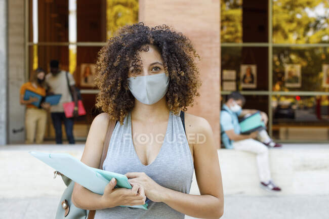 Young woman with documents wearing protective face mask while standing in university campus — Stock Photo