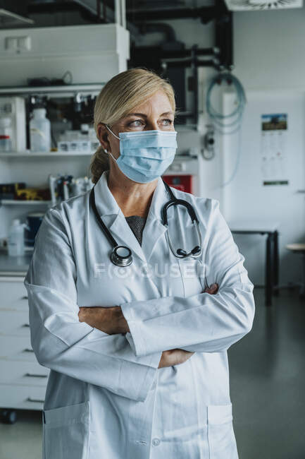 Scienziato indossando maschera in piedi con le braccia incrociate in laboratorio — Foto stock