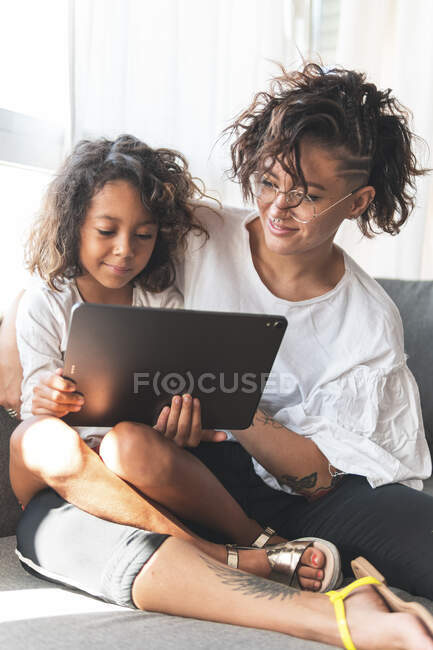 Mother and daughter sitting together on sofa with digital tablet — Stock Photo