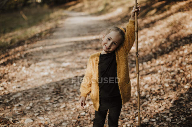 Девушка улыбается, держа палку, стоя на лесной тропе — стоковое фото