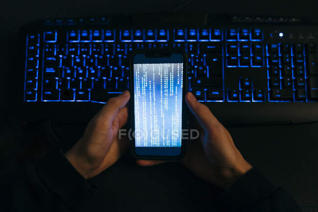Computer hacker hand holding mobile phone against computer keyboard at office — Stock Photo