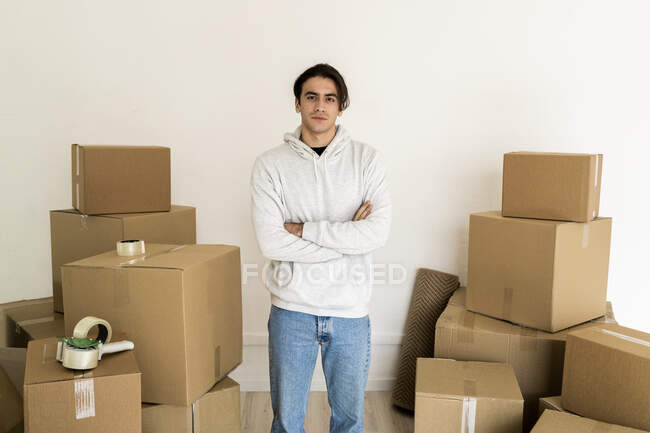 Giovane con le braccia incrociate in piedi tra scatole di cartone in una nuova casa — Foto stock