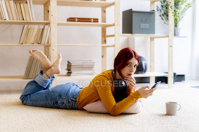 Donna rossa che utilizza il telefono cellulare mentre si trova sul tappeto a casa — Foto stock