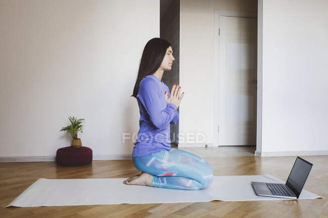 Mujer adulta aprendiendo yoga a través de un portátil mientras está sentada en casa - foto de stock