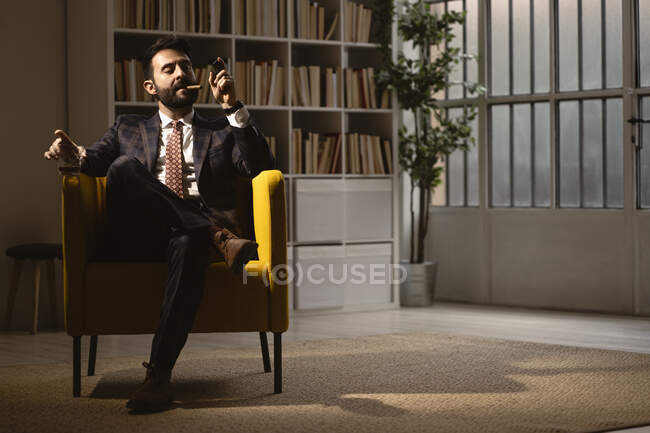 Ritratto di uomo ben vestito seduto in poltrona e godendo sigaro e bicchiere di whisky — Foto stock