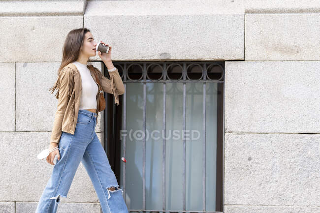 Jovem mulher bebendo café enquanto caminhava pela parede — Fotografia de Stock
