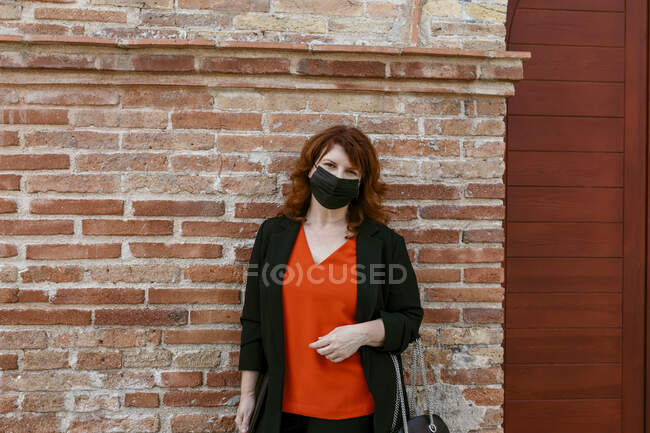 Femme avec masque protecteur debout contre un mur de briques en ville — Photo de stock