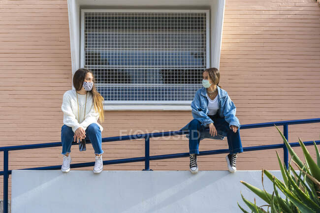Female friends looking at each other while sitting on railing — Fotografia de Stock