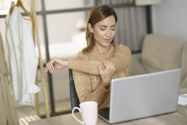 Empresária esticando a mão enquanto trabalhava no laptop em casa — Fotografia de Stock