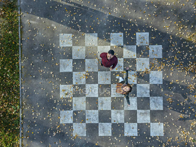 Mujer despreocupada con los brazos extendidos de pie por el hombre en el tablero de ajedrez pintado sobre asfalto - foto de stock