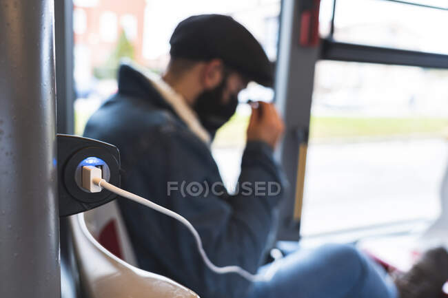 USB кабель підключений до електричної розетки в той час як бізнесмен на задньому плані в автобусі — стокове фото