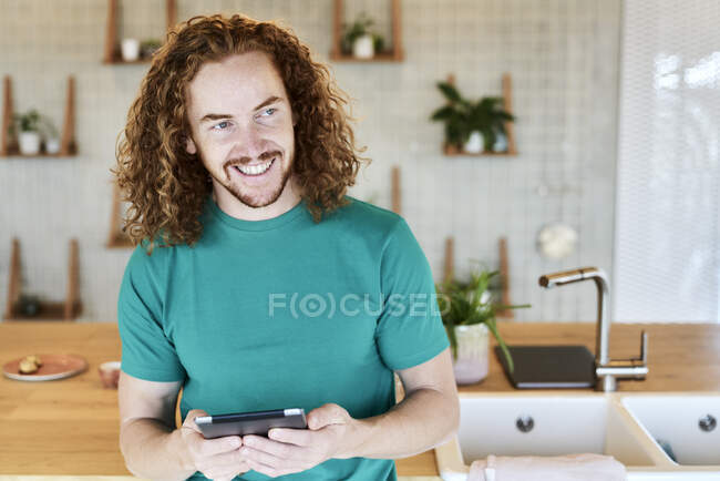 Smiling man looking away while using digital tablet in kitchen of studio apartment — Fotografia de Stock