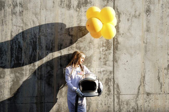 Chica sosteniendo globo de pie contra la pared en el día soleado - foto de stock