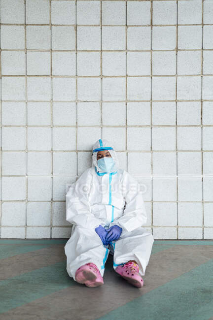 Thoughtful female nurse sitting against tiled wall — Photo de stock