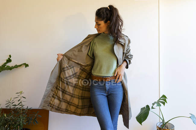 Modello femminile che indossa giacca in piedi contro parete a casa — Foto stock