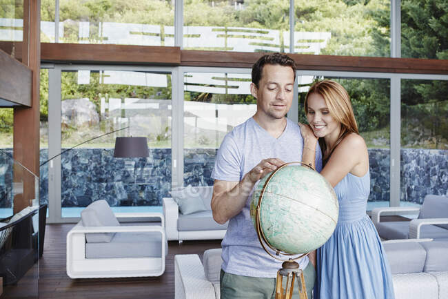 Пара смотрит на глобус, стоя в современном доме — стоковое фото