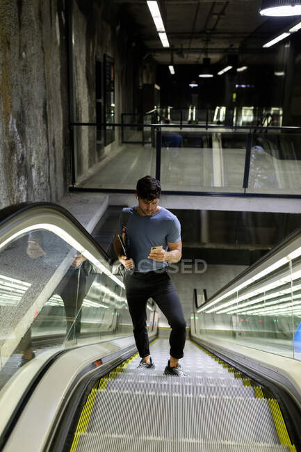 Hombre viajero utilizando el teléfono móvil, mientras que de pie en escaleras mecánicas en movimiento en el metro - foto de stock