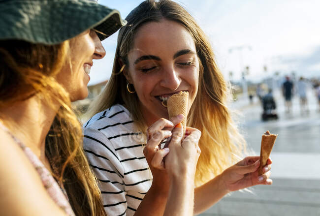 Усмішка молодої жінки годує сестричку морозивом, а в місті вона проводить час. — стокове фото