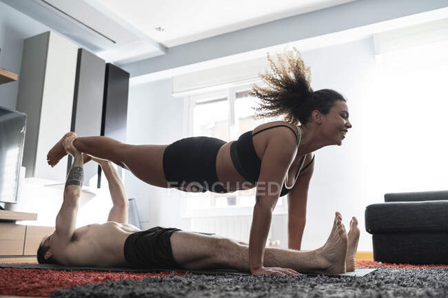 Mann hält Frau Bein, während sie zu Hause auf Teppich liegt — Stockfoto
