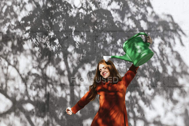 Woman holding watering can up while standing against tree shadow wall — Stock Photo