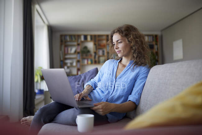 Mid adult woman using laptop while sitting on sofa at home — Stock Photo
