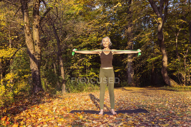 Mature woman exercising with resistance band at park during autumn — Foto stock