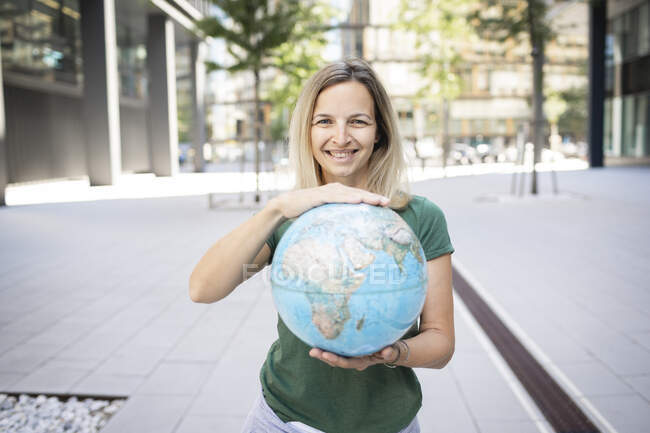 Donna sorridente che tiene il globo mentre in piedi sul sentiero in città — Foto stock