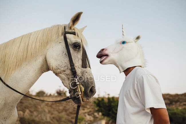 Caballo blanco y hombre con máscara de unicornio mirándose - foto de stock