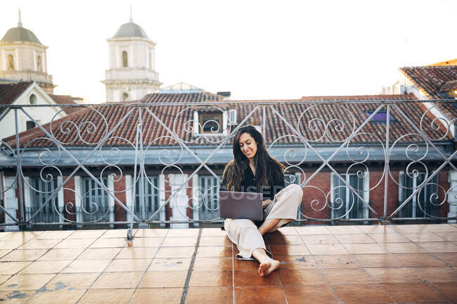 Молода жінка користується ноутбуком, сидячи на терасі з ясним небом. — стокове фото
