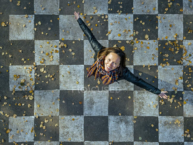 Smiling woman with arms outstretched spinning on asphalt painted with checked pattern — Stock Photo