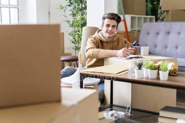 Smiling man with pen holding mobile phone over box in new apartment — Stock Photo
