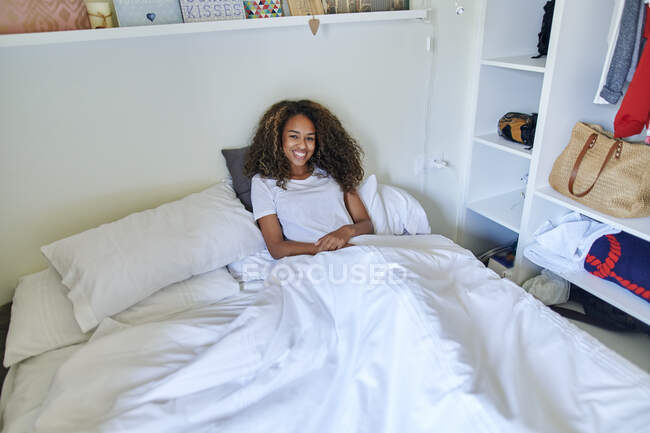 Glückliche junge Frau liegt auf dem Bett, während sie zu Hause im Schlafzimmer relaxt — Stockfoto