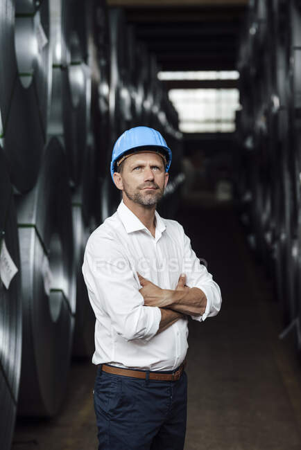 Uomo d'affari che contempla con le braccia incrociate in piedi da rulli in acciaio in fabbrica — Foto stock