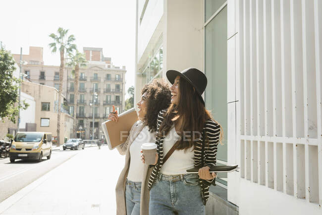 Businesswomen laughing while looking away standing on street in city during sunny day — Stock Photo