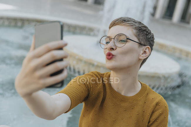 Femme adulte moyenne prenant selfie sur téléphone intelligent debout contre fontaine — Photo de stock