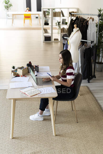 Jovem designer feminina usando laptop enquanto se senta em estúdio — Fotografia de Stock