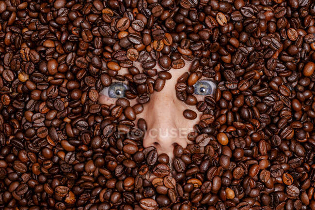 Cara humana enterrada en granos de café tostados - foto de stock