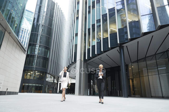 Professionnelles marchant avec des téléphones portables contre un immeuble de bureaux au centre-ville — Photo de stock