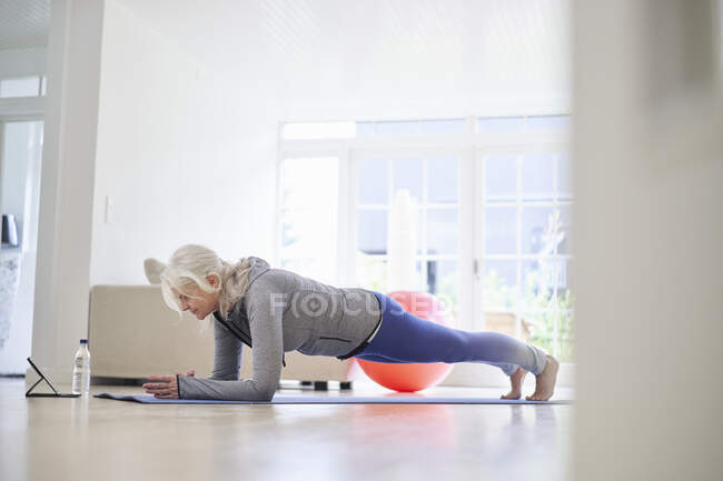 Active senior woman practicing plank position on mat at home — Stock Photo