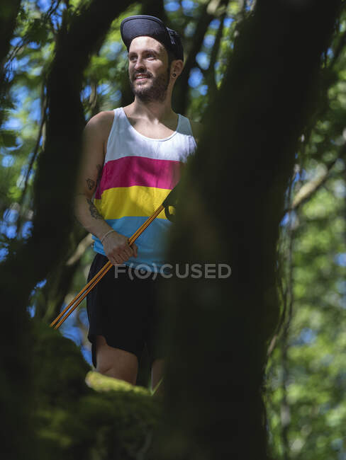 Atleta sosteniendo poste de senderismo mientras está de pie en el bosque - foto de stock