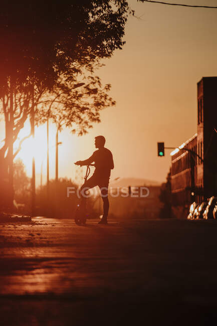 In silhouette of man standing with electric push scooter on road in city — Foto stock