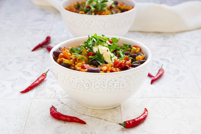 Bowl of vegetarian stew with red lentils, chili peppers, celery, kidney beans, tomatoes, carrots and sour cream — Stock Photo