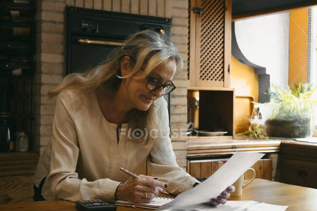 Frau berechnet Haushalt, während sie zu Hause in der Küche steht — Stockfoto