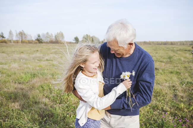 Buon nonno con nipote che tiene fiori di camomilla sul campo — Foto stock