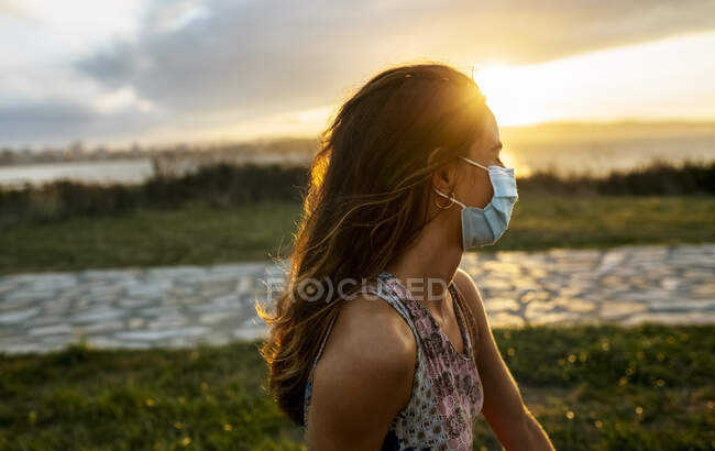 Молода жінка в захисній масці проти неба під час спалаху COVID-19 — стокове фото