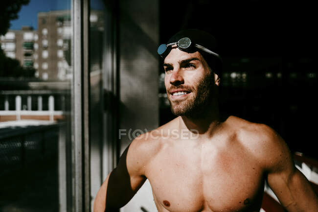Nuotatore maschio sorridente senza maglietta in piedi vicino alla finestra — Foto stock
