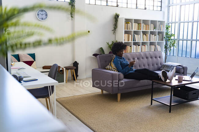 Young woman using mobile phone while resting on sofa at home — Stock Photo
