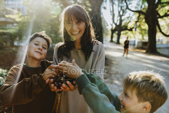 Sorridente madre e figli a raccogliere castagne mentre in piedi nel parco pubblico — Foto stock