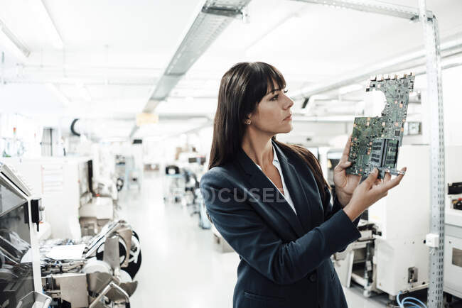 Mujer de negocios investigando mientras mira la placa de circuito en la industria - foto de stock