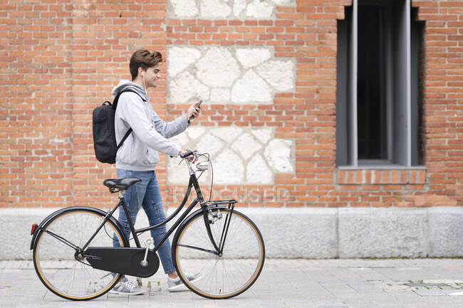Smiling man on video call wheeling bicycle by building — Stock Photo